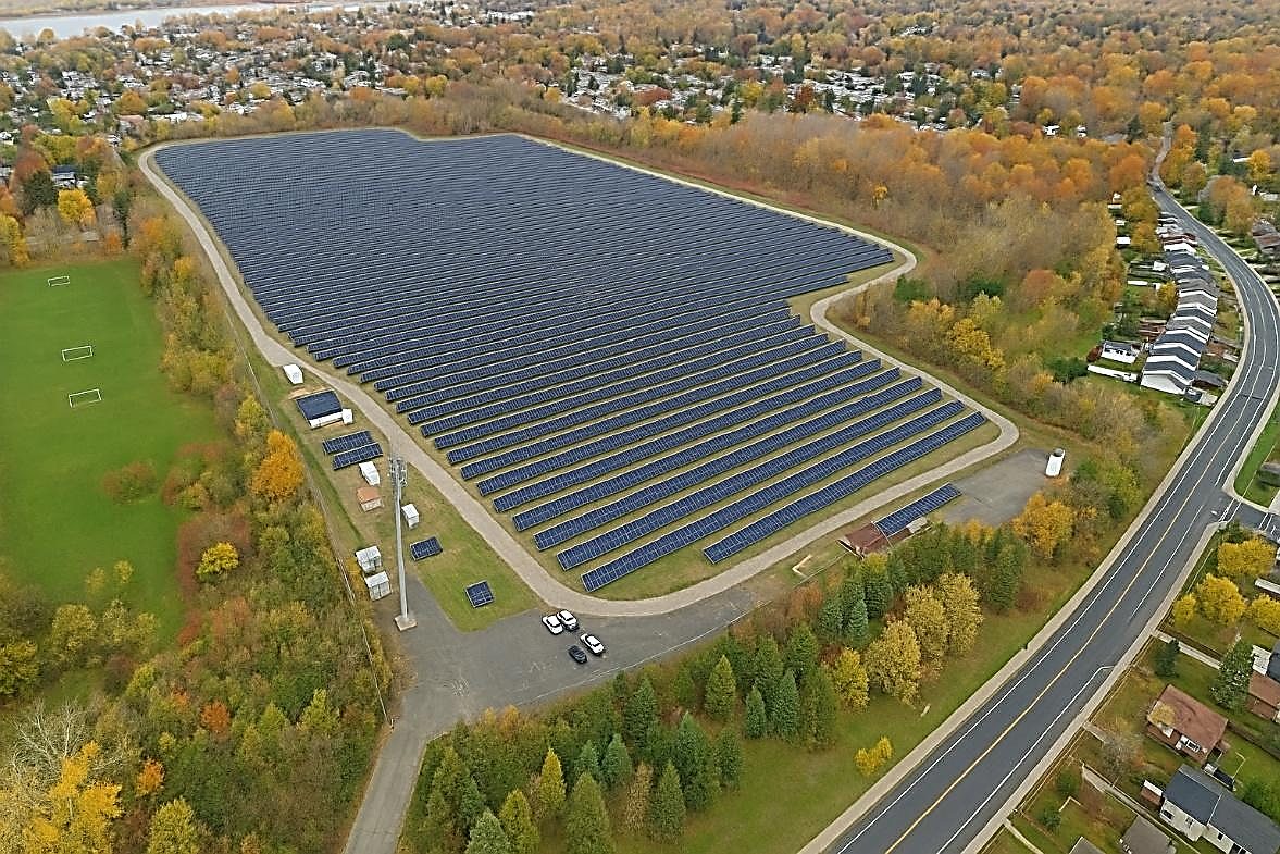 Exemple de centrale photovoltaïque au sol intégrée en milieu périurbain, bordée d’arbres et de résidences